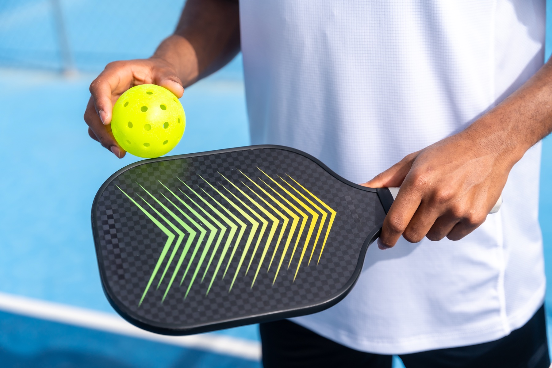 Pickleball player holding a paddle and bright yellow ball on a blue court