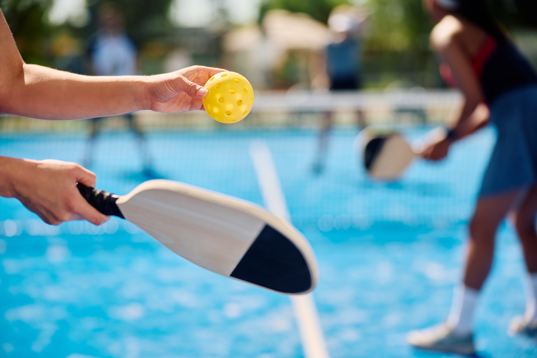 Player preparing to serve a yellow pickleball on a blue court
