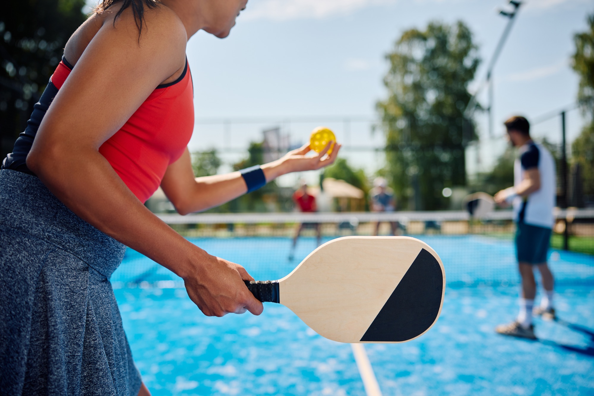 Player preparing to serve a yellow pickleball on a bright blue court