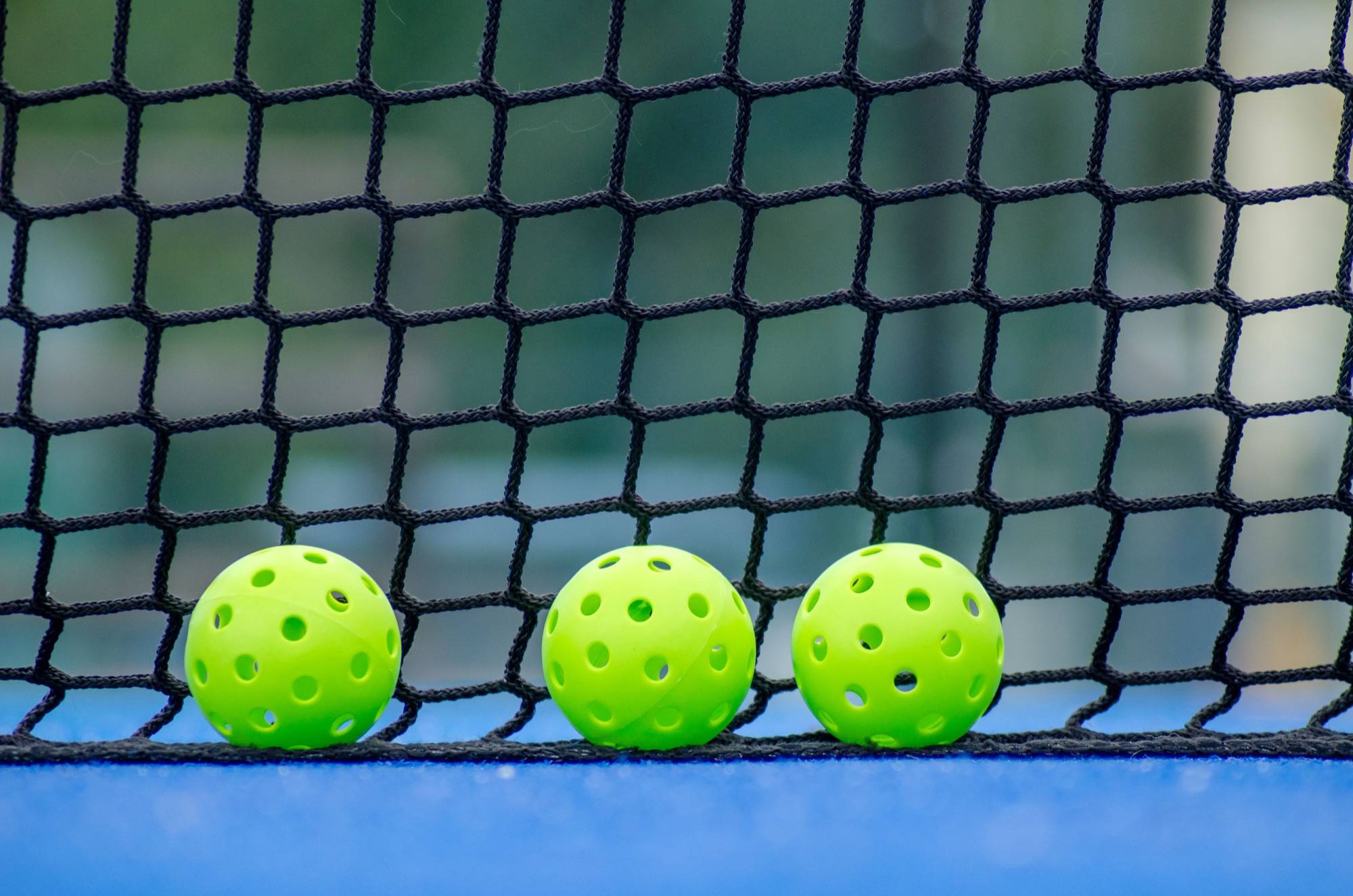 Three green pickleballs beside the net
