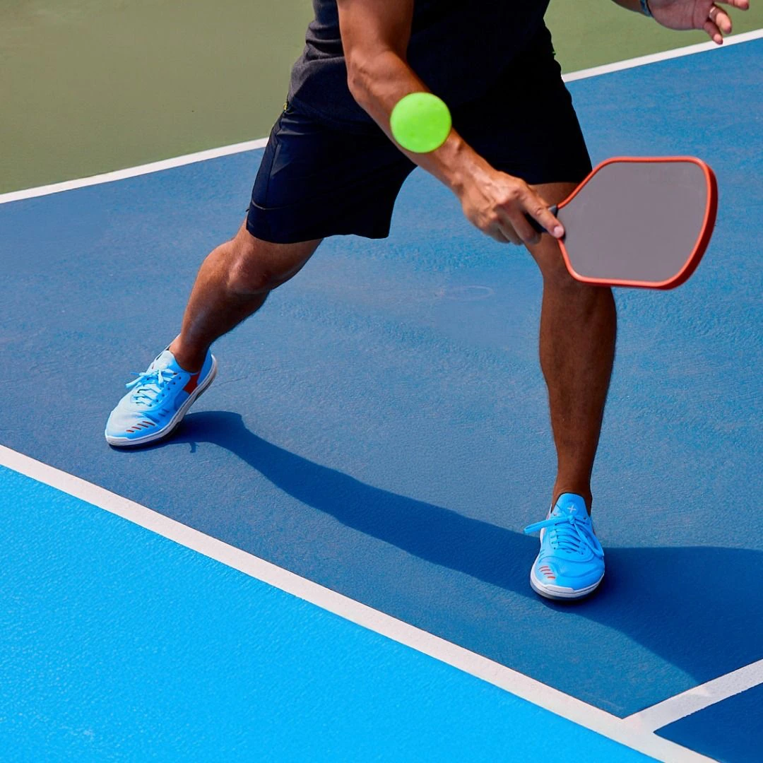 Player reaching for a green pickleball on a blue court