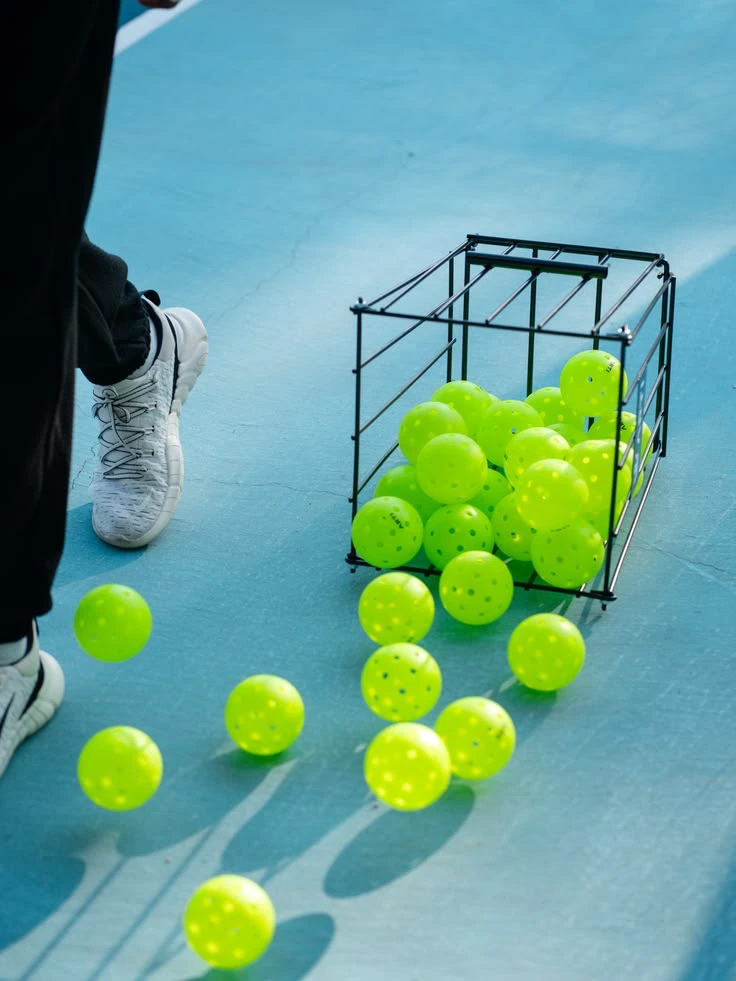 Yellow pickleballs spilling from a training basket